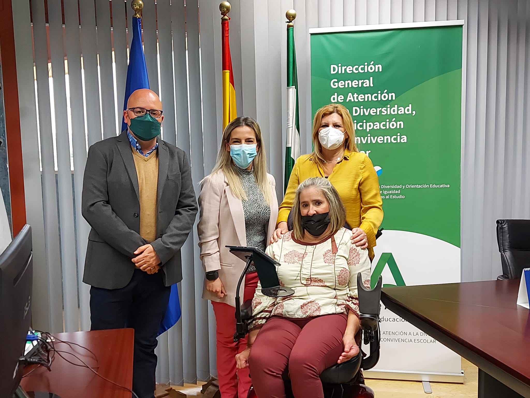 Tres personas en pie y una en silla de ruedas posan en foto de familia.