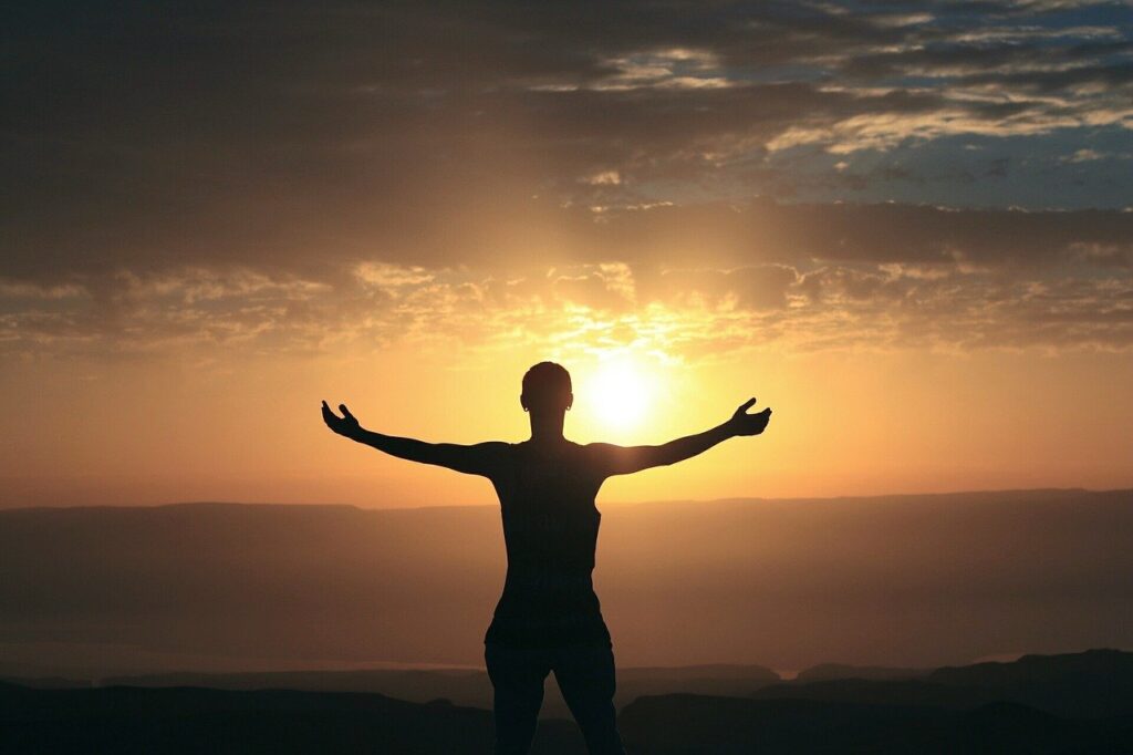 mujer con los brazos abiertos mirando una puesta de sol