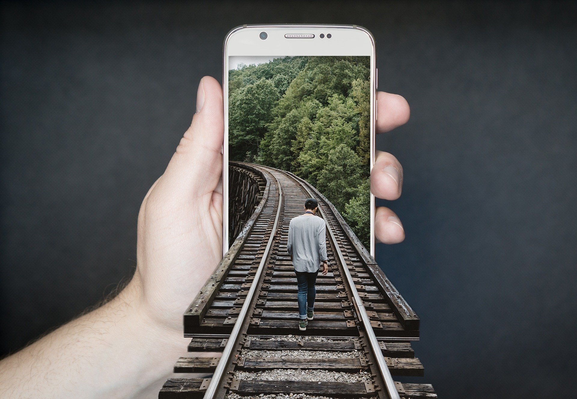 Teléfono móvil del que sale una vía de tren y sobre ella camina un hombre.