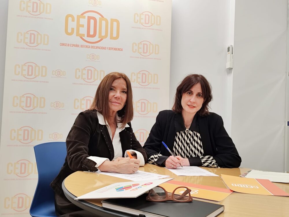 Dos mujeres sentadas a una mesa, firmando unos papeles.