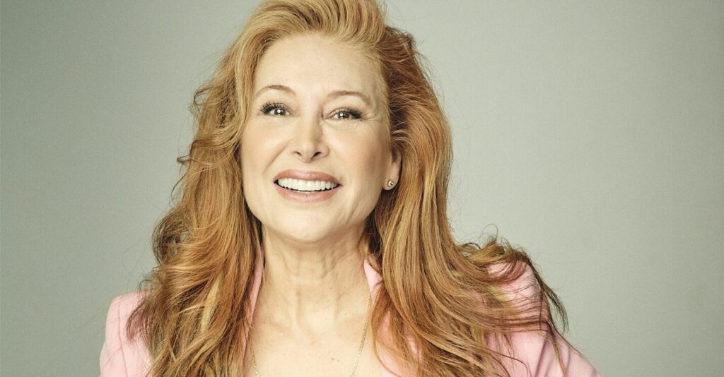 una mujer rubia, de pelo largo, con chaqueta rosa y camisa blanca