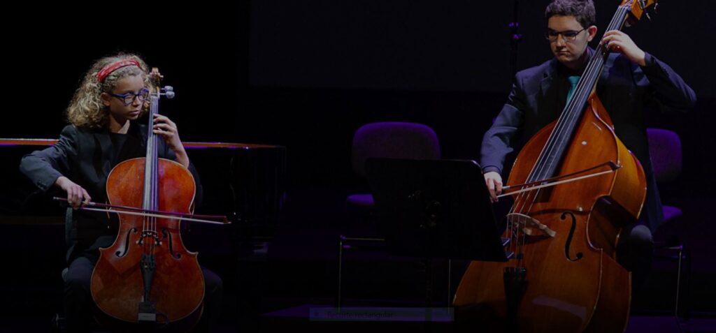 captura de una foto de las becas Super Arte. En ella se ve a una niña y a un joven tocando el violonchelo