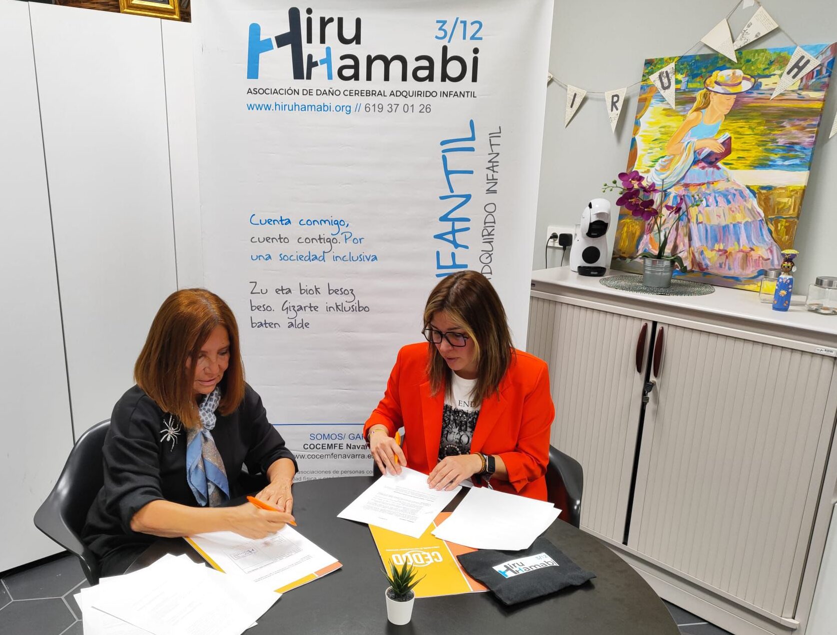 dos mujeres, sentadas a una mesa, firmando unos papeles