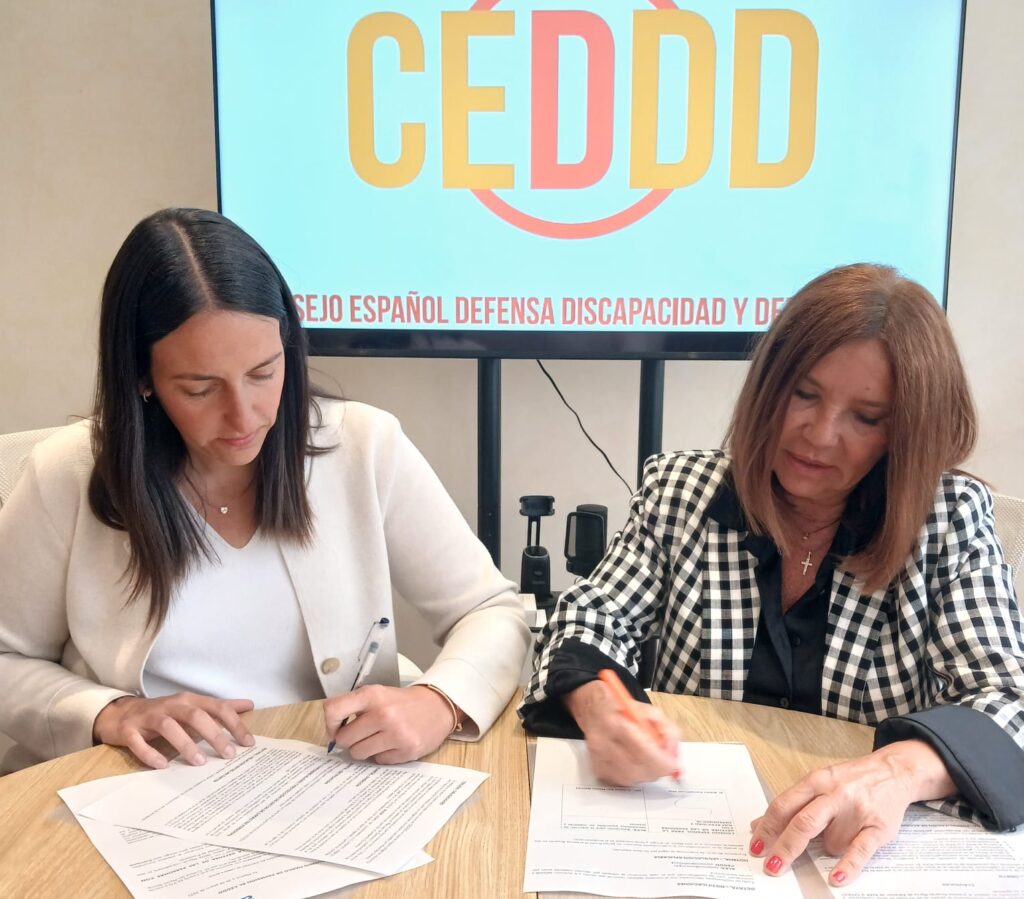 dos mujeres, sentadas a una mesa, firmando papeles.