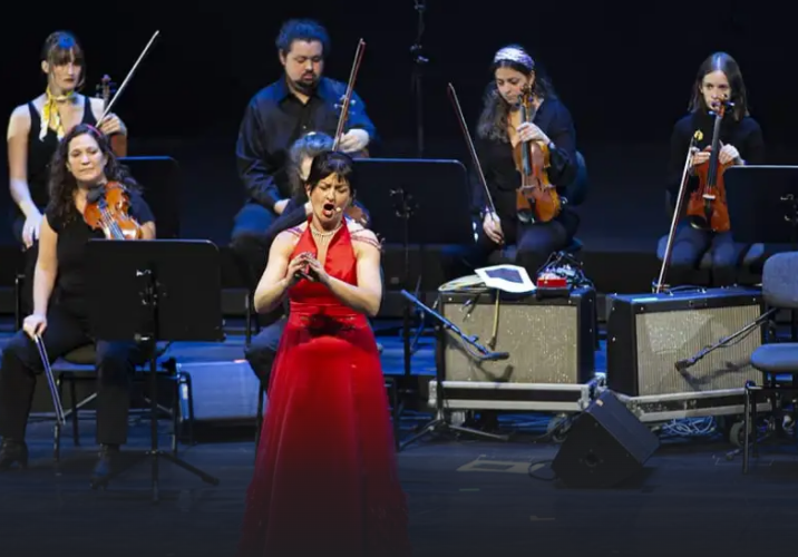 una mujer con un vestido rojo sobre un escenario, con músicos detrás.